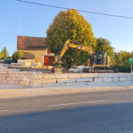 Mise en œuvre avec une pelleteuse Caterpillar 315d e blocs d'enrochement de Limeyrat provenant de la carrière de Montagnac d'auberoche pour l'aménagement des espaces autour du bureau de tabac à Fossemagne par l'entreprise SARL TCTP en Dordogne