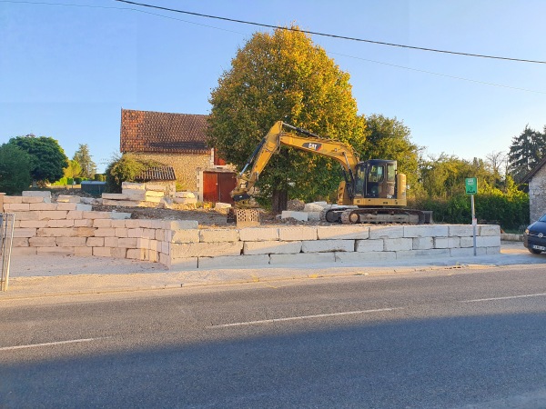 Mise en œuvre avec une pelleteuse Caterpillar 315d e blocs d'enrochement de Limeyrat provenant de la carrière de Montagnac d'auberoche pour l'aménagement des espaces autour du bureau de tabac à Fossemagne par l'entreprise SARL TCTP en Dordogne
